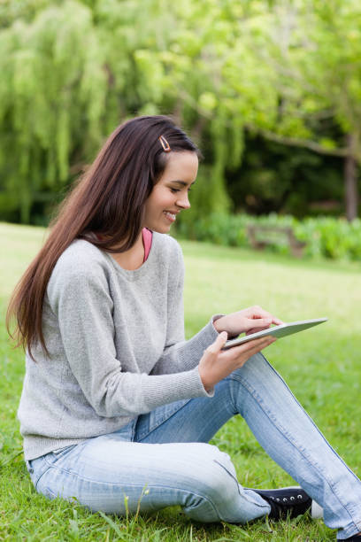 istock Smiling young girl using her tablet pc while sitting in a park 825275914