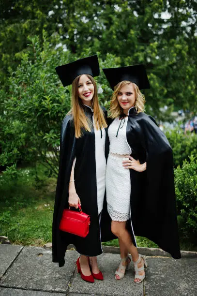 Photo of Two amazing young female graduates standing outside in graduation gowns and caps.