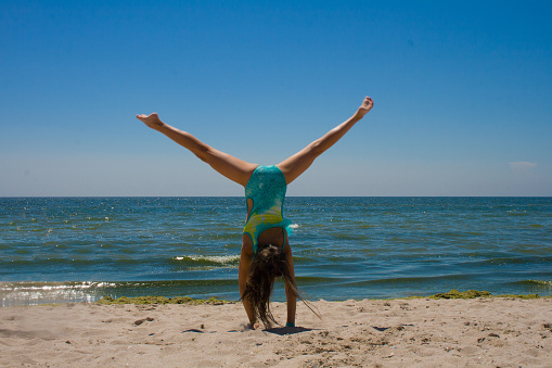 A teenage girl makes an acrobatic wheel against the background of the sea on a summer sunny day