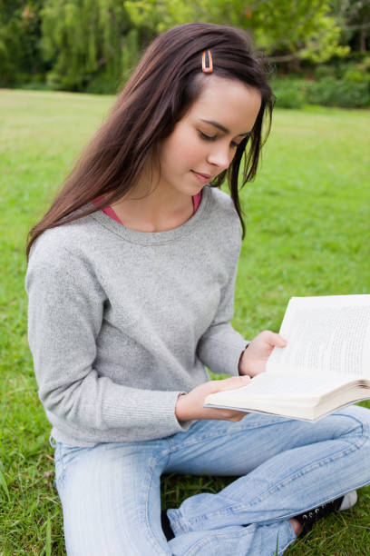 istock Young calm girl reading a book while sitting on the grass 825291446