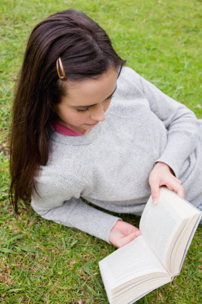 istock Young woman reading a book while lying on the grass 825291544
