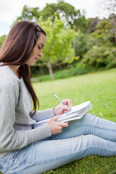 istock Side view of a young girl sitting on the grass while writing on her notebook 825291692