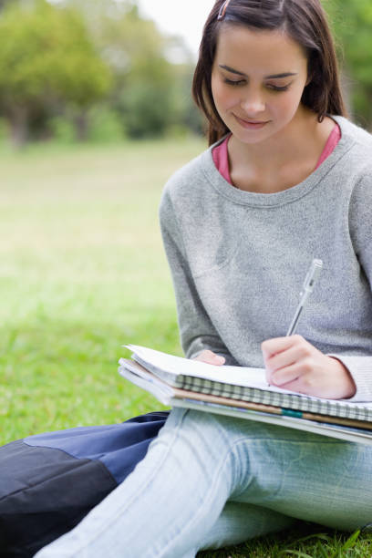 istock Young smiling girl writing on her notebook while sitting in a park 825291952