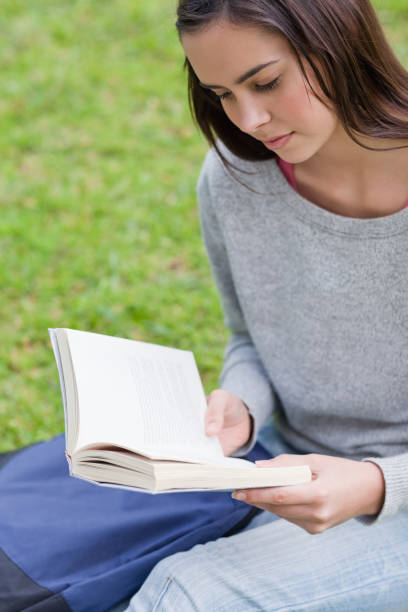 istock Young girl sitting on the grass while reading a book 825292002