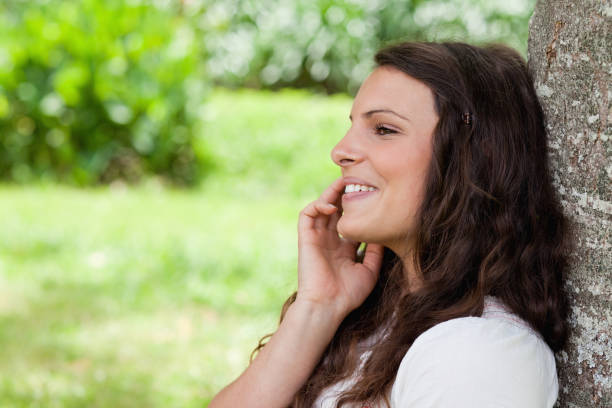 istock Smiling woman leaning against a tree while talking on the phone 825292300