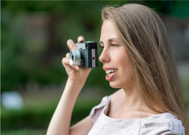 istock Beautiful woman is taking picture with old fashioned camera, outdoors. 825299544
