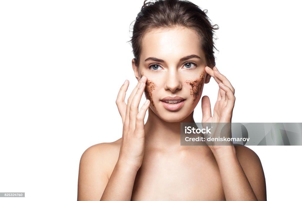 Portrait of a young woman with a coffee scrub on her face doing peeling skin isolated on white background Exfoliation Stock Photo
