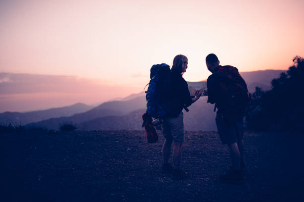 Senior mother and son hiking on mountain reading a map for directions after sunset