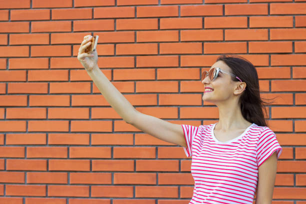 istock Beautiful stylish girl making selfie on brick wall background 825355254