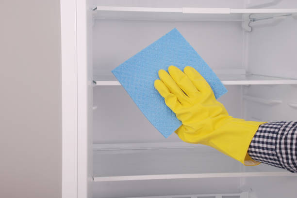 istock Young girl cleaning empty fridge with a sponge. 825359312
