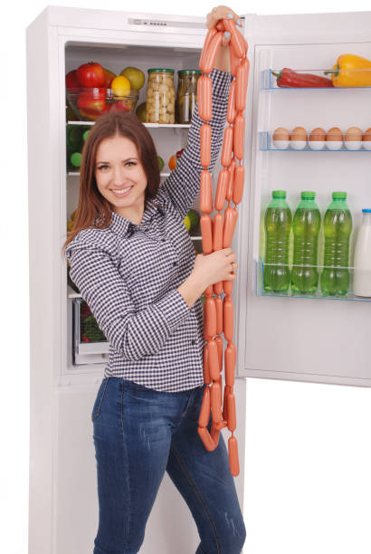 istock Young girl holds sausages on the refrigerator background 825367268