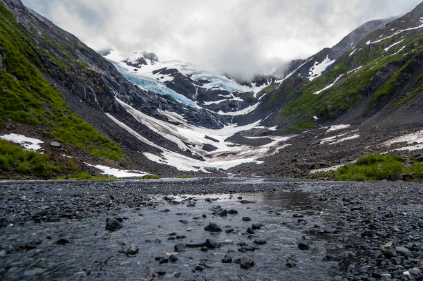View of the Byron Glacier and Byron creek with stones View of the Byron Glacier on the background and Byron creek in the foreground with multiple rocks and blurred reflection of snow in the water. Shot in the USA, Alaska. portage valley stock pictures, royalty-free photos & images