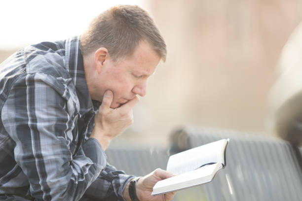 istock Man sitting on bench with Bible 825375024