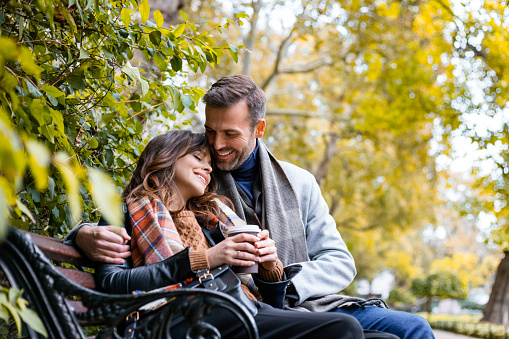 Beautiful smiling couple sitting relaxed on park bench. Couple in love spending time with each other.
