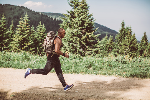 One man, running in nature alone, wearing a backpack.