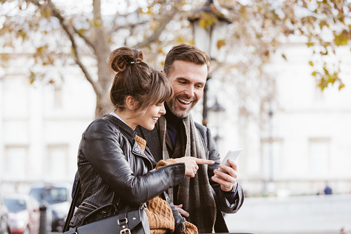 Smiling couple using mobile phone outdoors in the city. Woman pointing at smart phone.