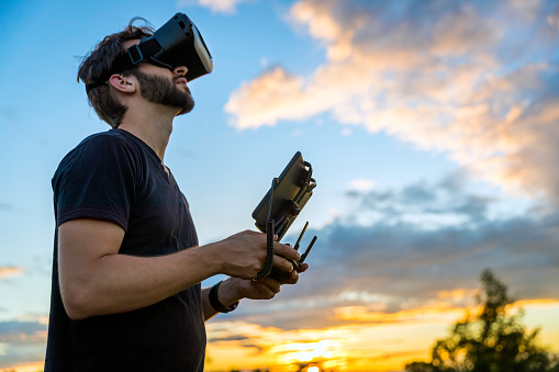 Man Flying a Drone with Virtual Reality Goggles Headset in a field at sunset