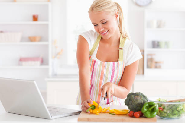 istock Close up of a blonde woman using a notebook slicing a pepper 825385758