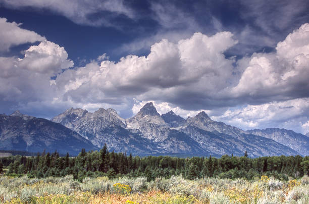 Scenic view of Grand Tetons under spectacular cloudy sky in baclground and sage brush in the foreground\n\n