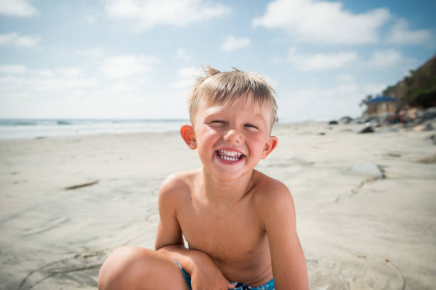 Blonde boy laughing at the beach, happy as can be.
