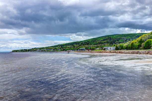 Saint Lawrence river shore, stormy waves and clouds with cityscape skyline and road of town village La Balbaie: Saint Lawrence river shore, stormy waves and clouds with cityscape skyline and road of town village charlevoix photos stock pictures, royalty-free photos & images