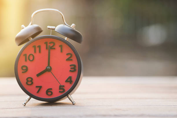 istock 8 o'clock retro alarm clock on wooden table outdoor with sunlight 825404928