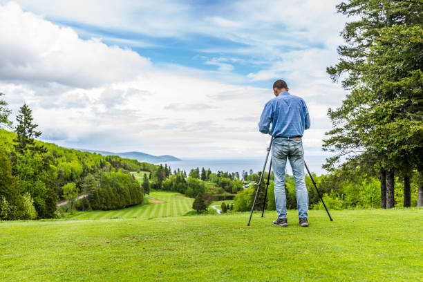 Landscape view of green golf course with hills in summer in La Malbaie, Quebec, Canada in Charlevoix region with photographer and tripod Landscape view of green golf course with hills in summer in La Malbaie, Quebec, Canada in Charlevoix region with photographer and tripod charlevoix photos stock pictures, royalty-free photos & images