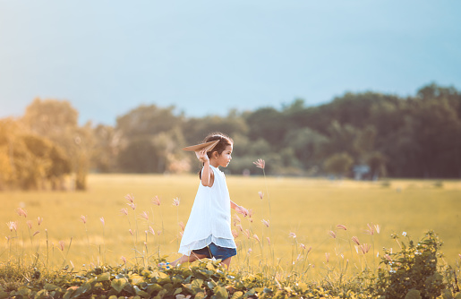 Cute asian child girl running and playing toy paper airplane in the field in vintage color tone