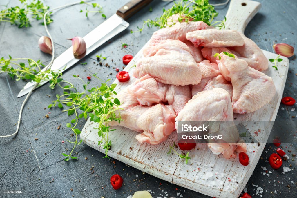 Fresh raw chicken wings on a white cutting board with thyme, chilli, salt, pepper, garlic Fresh raw chicken wings on a white cutting board with thyme, chilli, salt, pepper, garlic. Chicken Wing Stock Photo