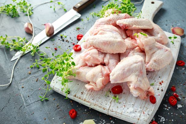 Fresh raw chicken wings on a white cutting board with thyme, chilli, salt, pepper, garlic Fresh raw chicken wings on a white cutting board with thyme, chilli, salt, pepper, garlic. raw food stock pictures, royalty-free photos & images