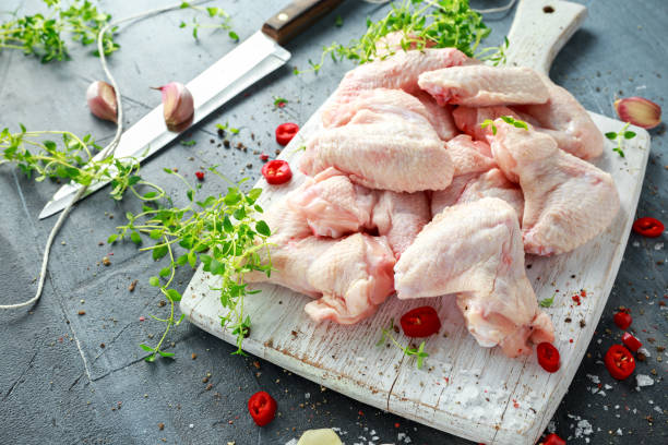 fresh raw chicken wings on a white cutting board with thyme, chilli, salt, pepper, garlic - pink pepper fotos imagens e fotografias de stock