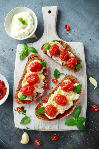 istock Tomato Ricotta Bruschetta with sun dried tomatoes paste, olive oil brown bread and basil in a white wooden board. 825461414