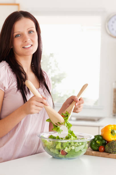 istock Smiling woman mixing a salad looking into the camera 825467590