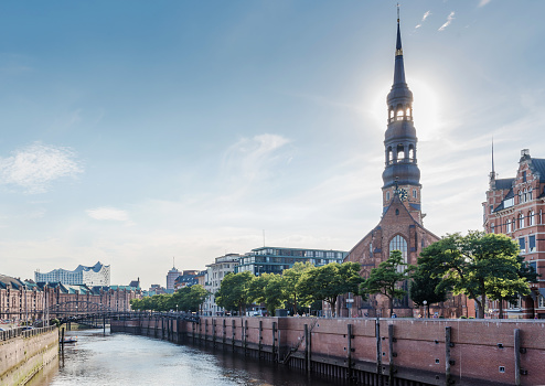 old warehouse district Speicherstadt in Hamburg, Germany under clear summer sky as seen from Zollkanal channel with with Sankt Katherinen church and Elbphilharmonie in background
