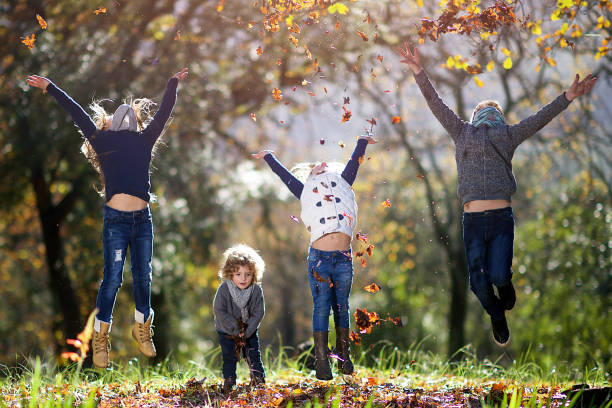istock Four siblings throwing autumn leaves in the air whilst jumping 825522742