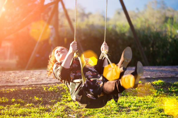 istock Woman swings on a tree swing with sun flare 825527216