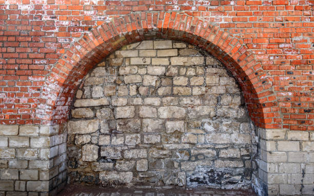 Close-up of an ancient brick wall featuring a partially damaged arch design, showcasing rustic textures, weathered surfaces, and traditional construction techniques. The uneven placement of bricks and faded mortar reflect the passage of time and the charm of heritage architecture. This detailed image highlights the raw beauty of aged structures, making it suitable for themes of history, architecture, construction, texture, and cultural heritage.