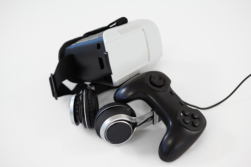 Close-up of joystick, virtual reality headset and headphones on white background