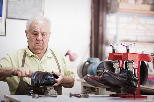 Senior cobbler repairing old shoes with knife. Portrait of a senior shoemaker. Shoemaker at work. Serbia, Europe