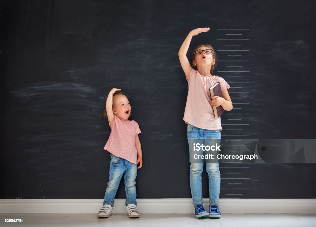 sisters play together Two children sisters play together. Kid measures the growth on the background of blackboard. Concept of education. Growth Stock Photo