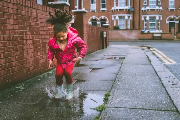 Photo of Child (5-6) in blue boots jumping in puddles.