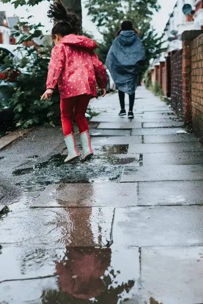 Stock photo of little girl who are having fun by jumping in puddles. This file has a signed model release.