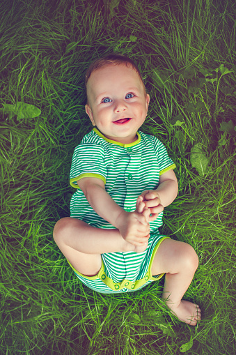 Cute baby boy laying on grass in summer