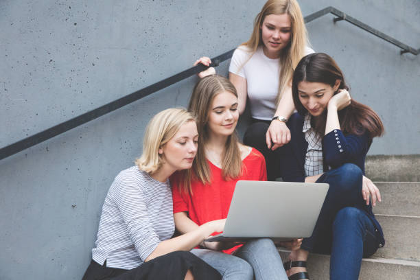 istock young female friends using technologies while sitting on steps outdoors 825586214
