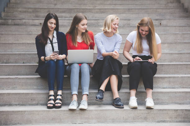 istock Young female friends using technologies while sitting on steps outdoors 825586308