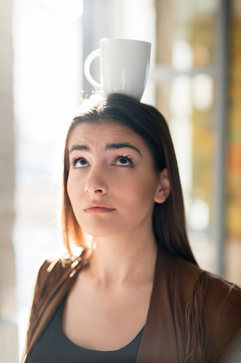 Portrait of a beautiful young woman balancing a coffee cup on her head.