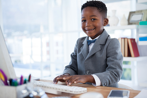 Portrait of boy imitating as businessman using computer at desk in office