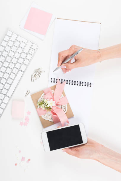 istock woman holding smartphone with blank screen and taking notes at workplace 825600070