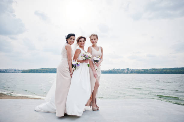 istock Stunning bride with pretty bridesmaids posing with bouquets on the lakeside. 825601060