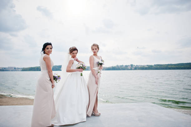 istock Stunning bride with pretty bridesmaids posing with bouquets on the lakeside. 825601092